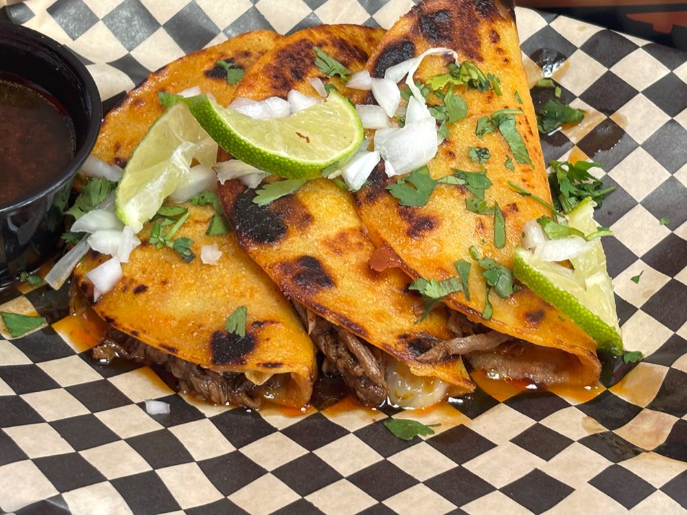 Close-up of crispy birria tacos with cilantro, onion, and lime served with consomé